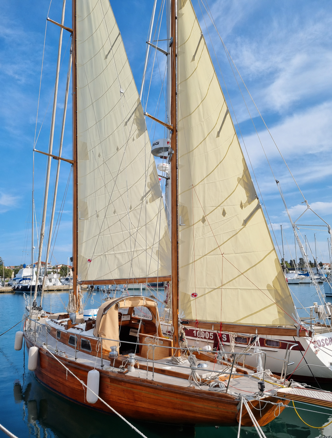 Classic 1965 wooden yawl moored in marina with sails set