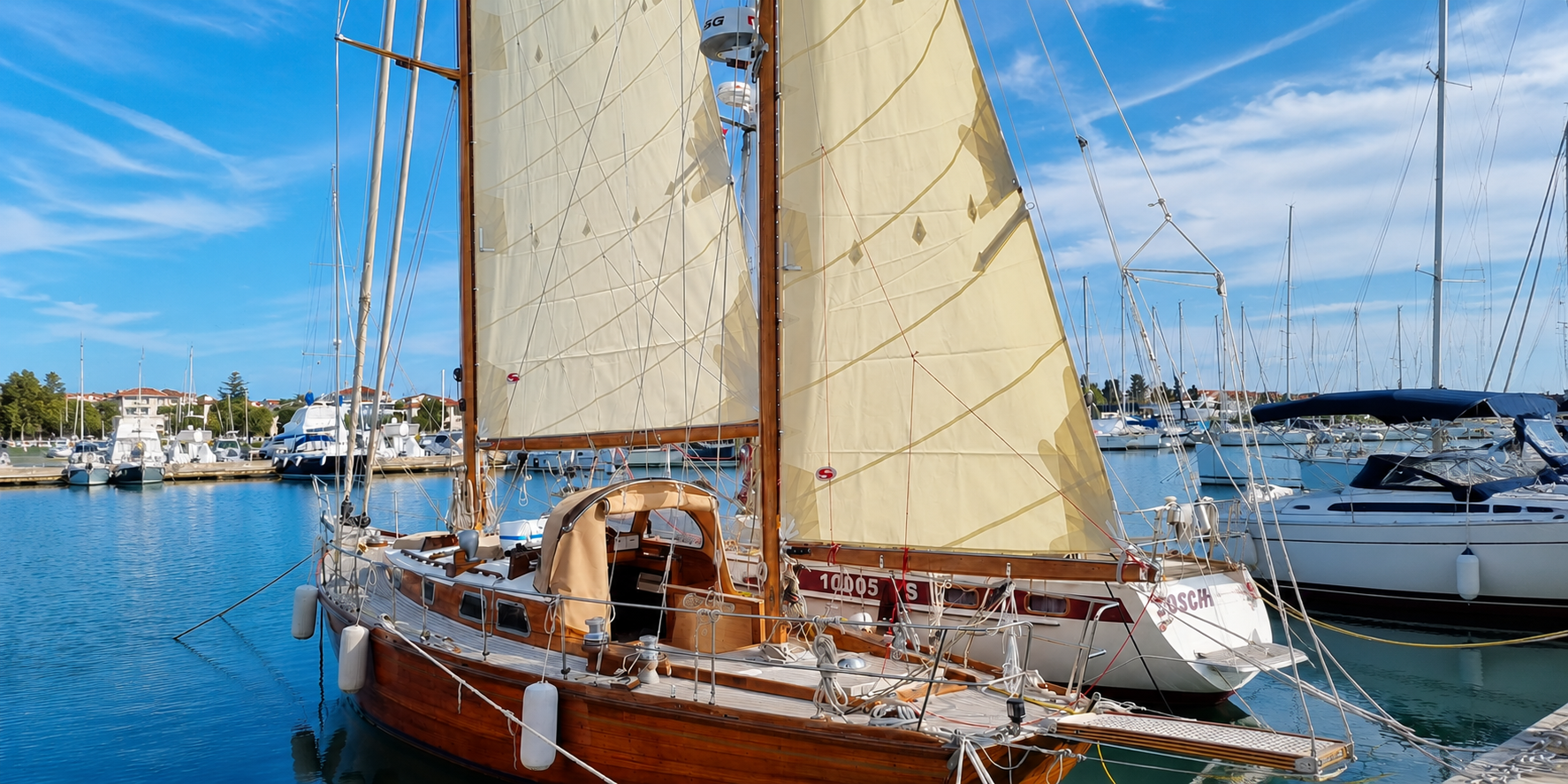 Classic 1965 wooden yawl with sails up, moored in marina